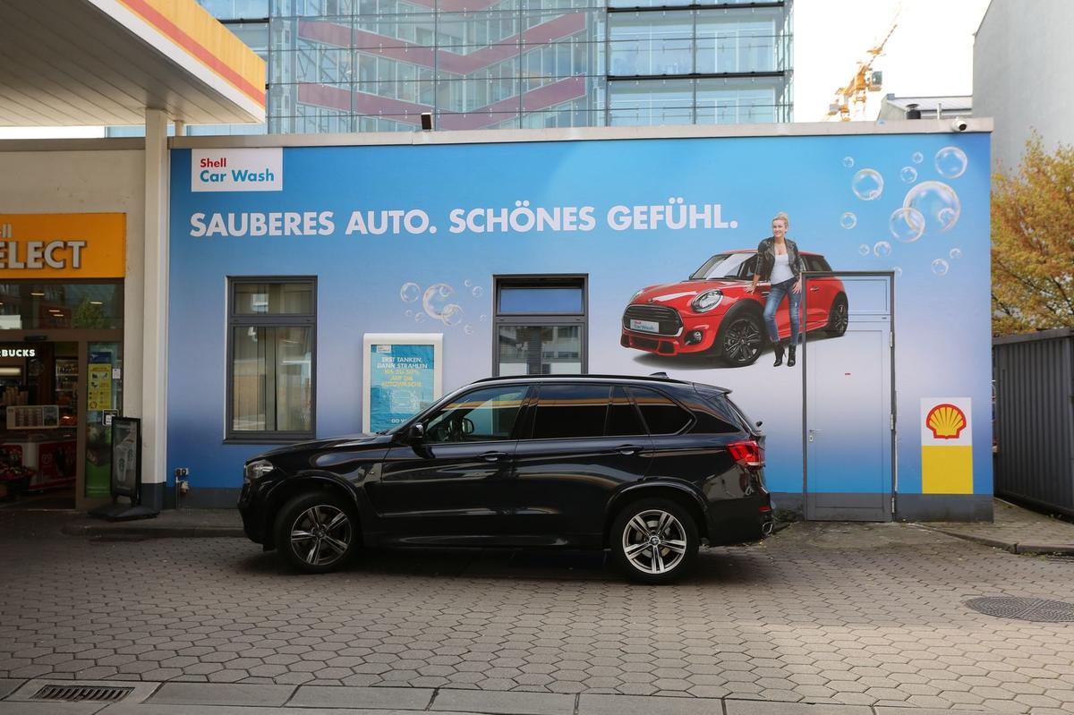 Großes Wandbanner an einem Gebäude einer Tankstelle mit Auto und Frau