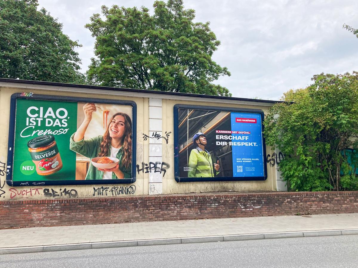 Zwei Werbeflächen an einer Mauer neben einer Straße